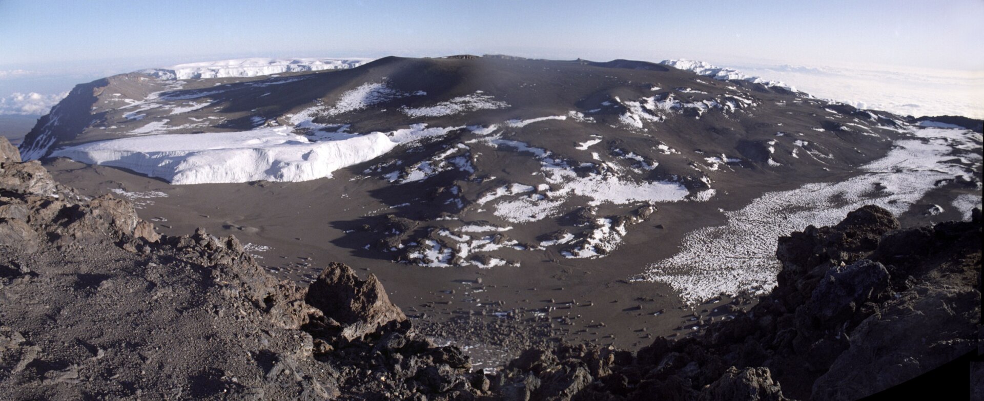 Weiter Blick über den Krater des Kibo mit Eisresten und Schneeflecken, vorn dunkler Fels